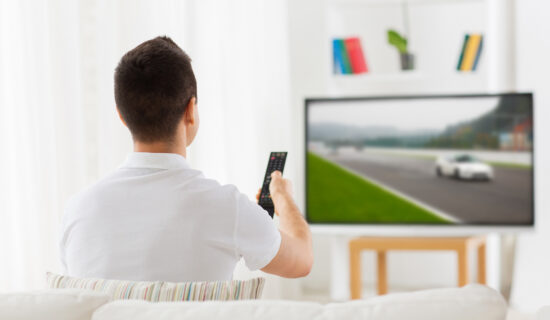 Man with remote watching motorsports on tv at home