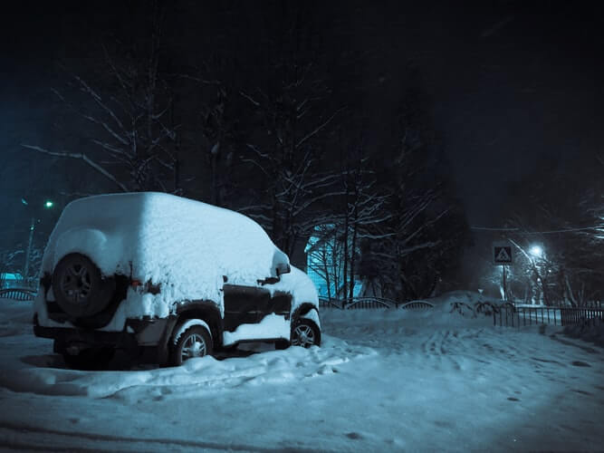 A snow covered SUV on the street during night-time