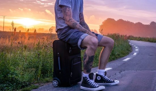 A guy sitting on a suitcase on the road