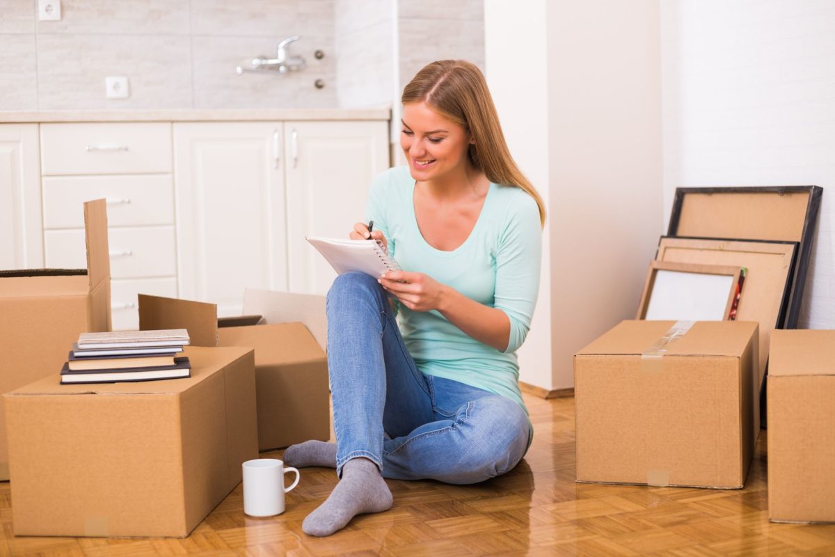 A girl sitting next to a box writing down her tasks for a long-distance move and auto transport