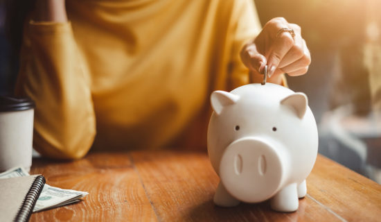 Woman inserting coin in piggy bank on table