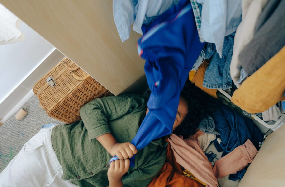 A girl lying under a pile of clothes