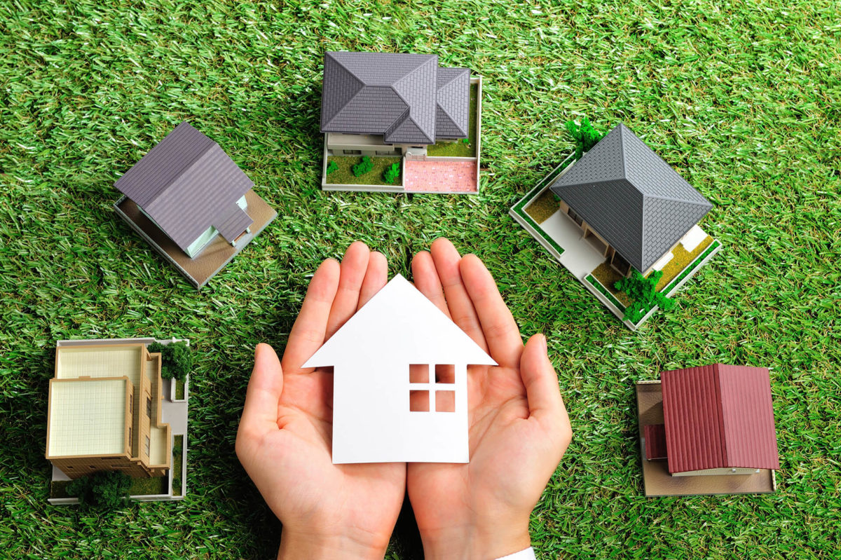 small models of various types of houses and two hands holding a little house cutout