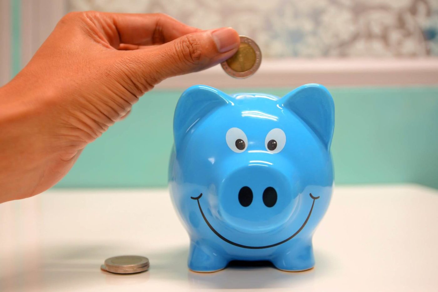 Person inserting coin in piggy bank on table