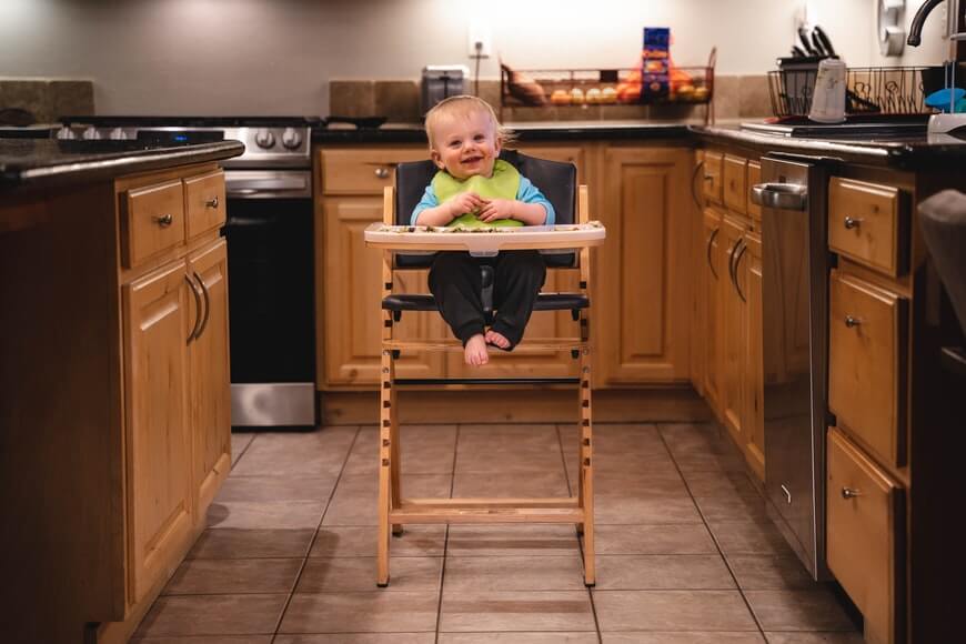 A smiling baby that is sitting in the chair in the kitchen