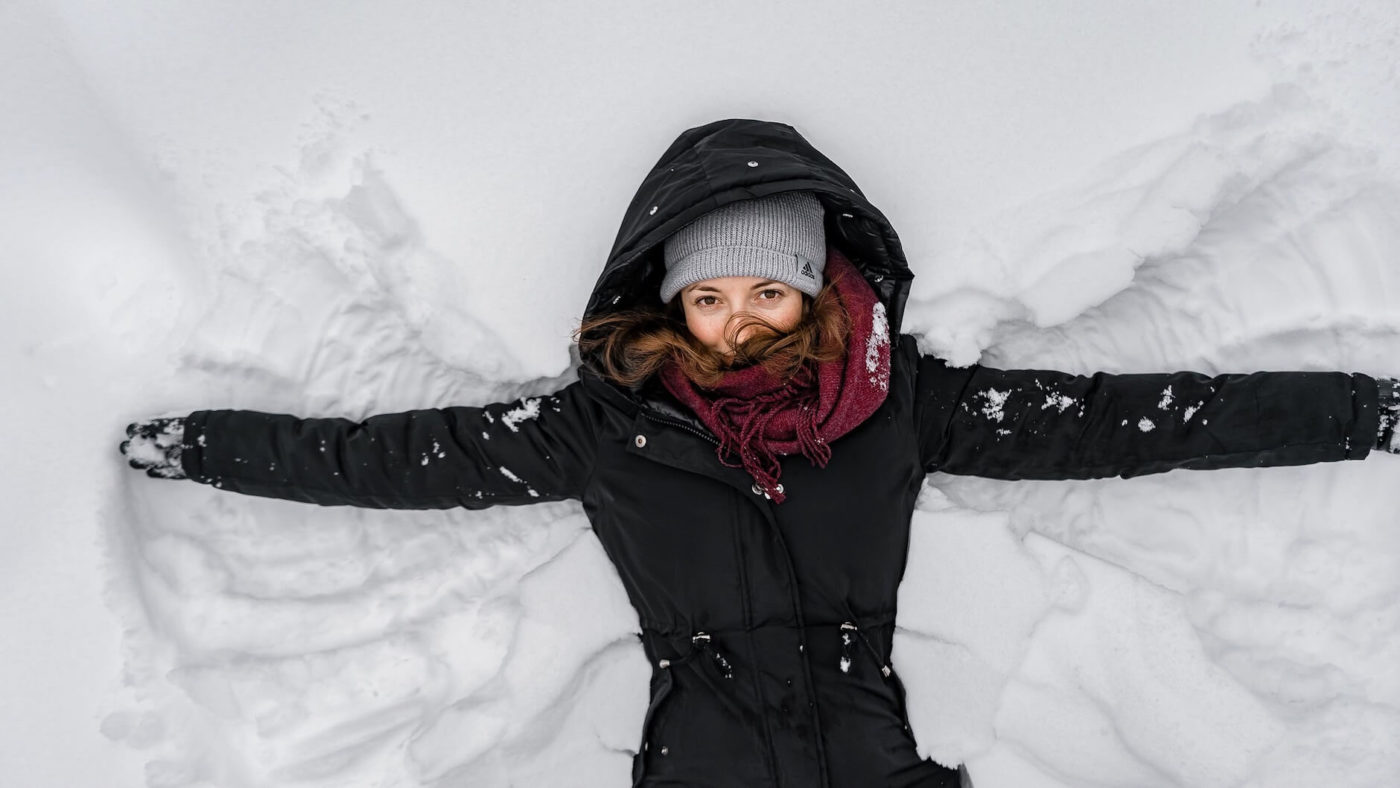 a girl wearing winter clothing and making a snow angel
