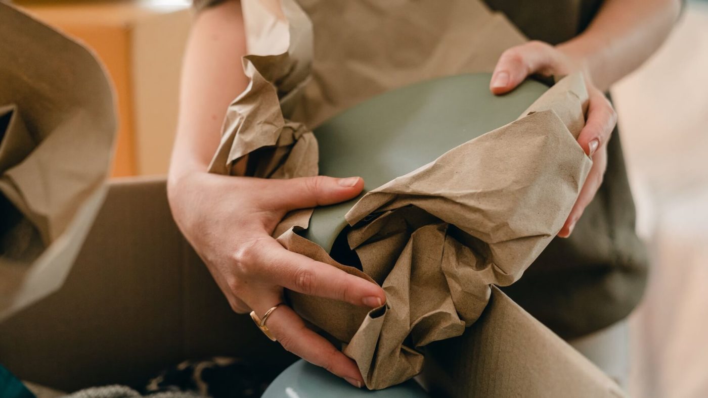 A woman wrapping up plates into packing paper