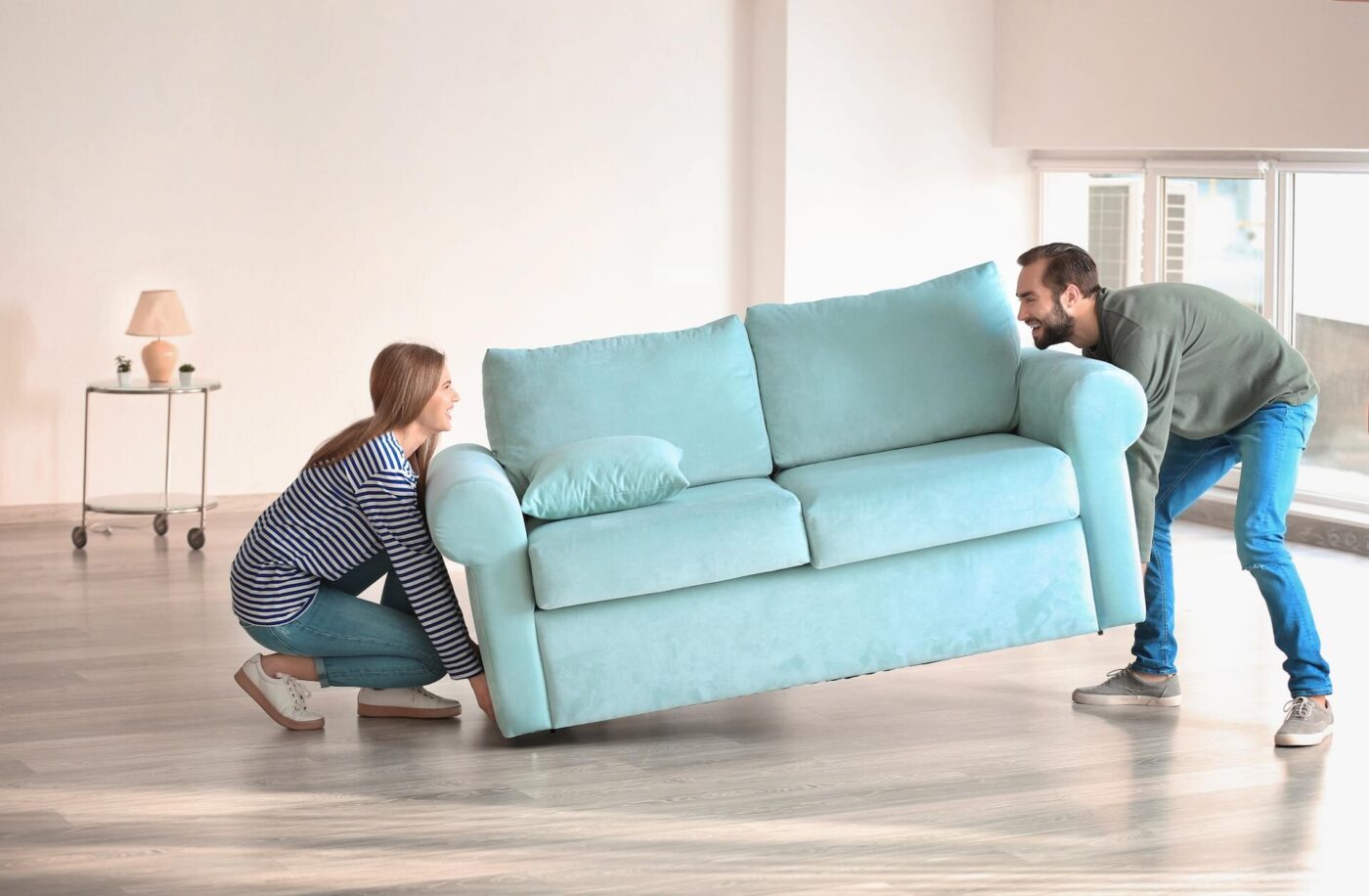 A man and woman lifting a turquoise sofa