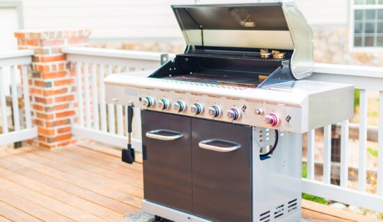 Six burner outdoor gas grill with open lid on backyard.