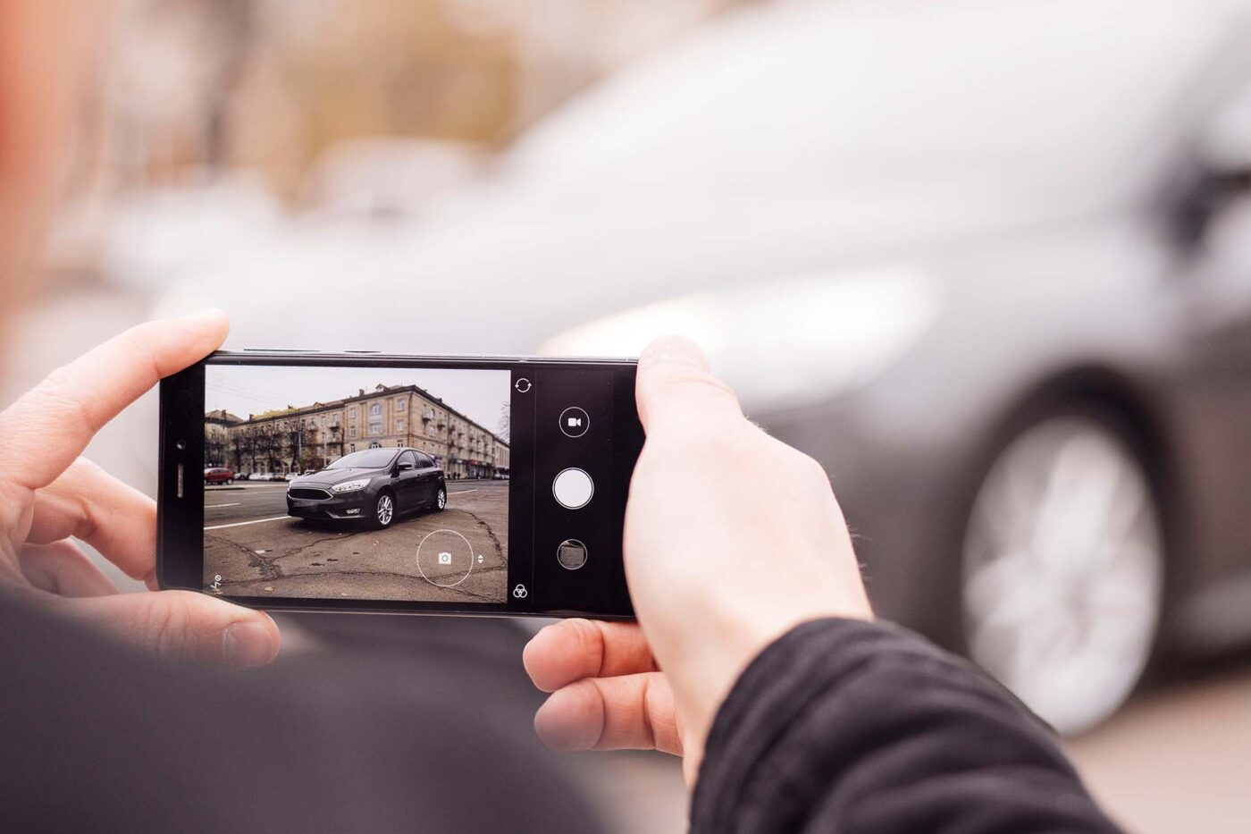 a man takes pictures of a car on the phone in the middle of the city