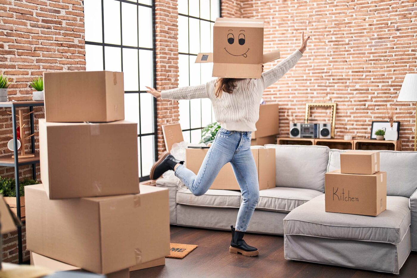 Young woman dancing with funny cardboard box on head at new home