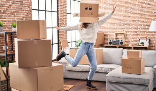 Young woman dancing with funny cardboard box on head at new home