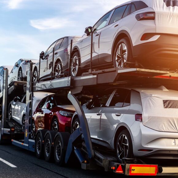 Tow truck car carrier semi trailer on highway carrying batch of new wrapped electric SUVs on motorway road at sunset evening time. Business distribution logistics service. Lorry driving highway.