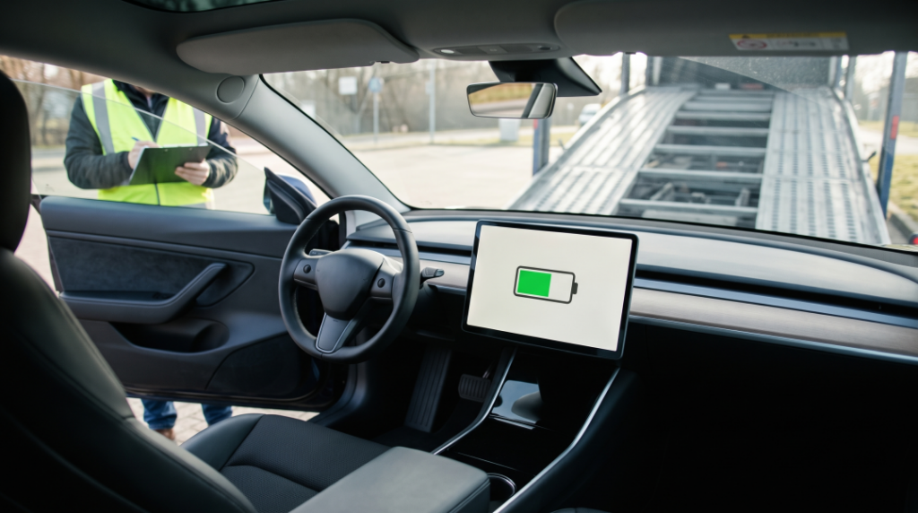 Driver documenting an electric car's partial battery charge on the dashboard screen before loading it onto a car carrier